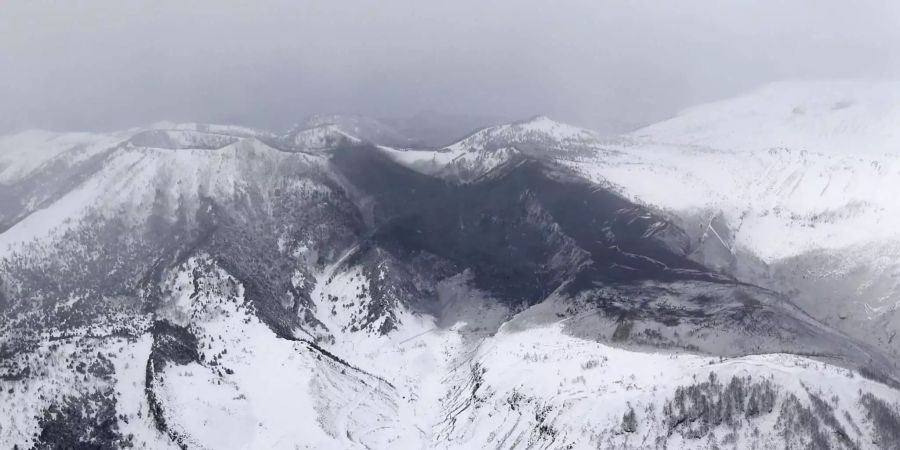 Asche des Vulkans Mount Kusatsu-Shirane liegt  nach einem Ausbruch auf Schneebedeckten Hängen neben dem Gipfel des Berges.