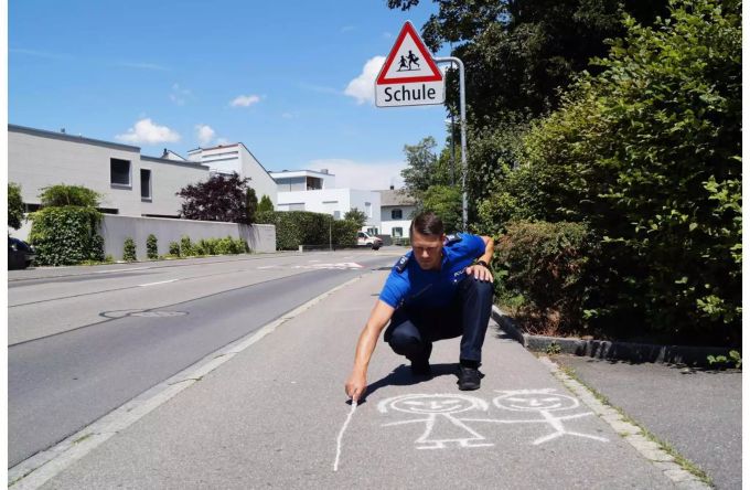 Polizist zeichnet mit Kreide symbolisch Kinder auf das Trottoir - zvg Kanton Zug Polizist zeichnet mit Kreide symbolisch Kinder auf das Trottoir - zvg Kanton Zug