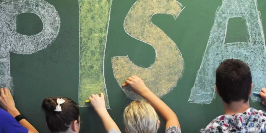 Schüler der malen in einem Gymnasium in Straubing (Niederbayern) das Wort «PISA» auf eine Tafel. Foto: Armin Weigel/dpa