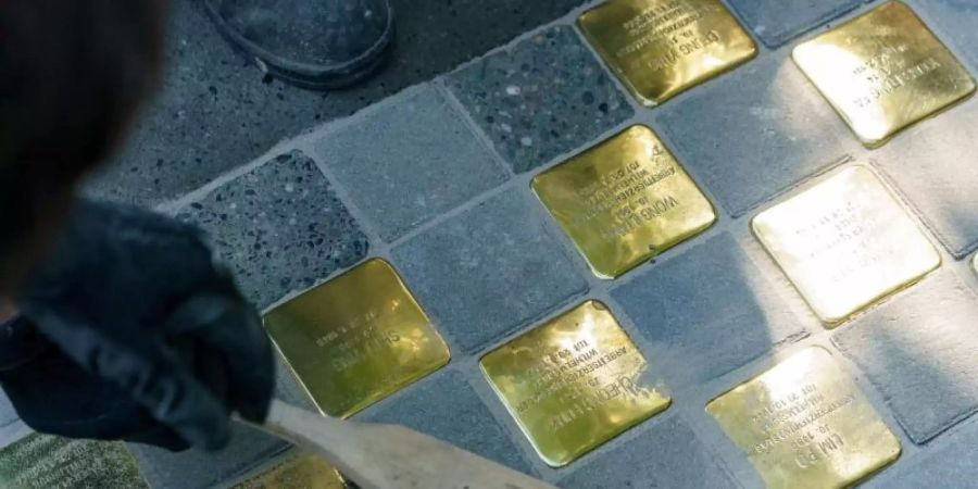 Künstler Gunter Demnig fegt die von ihm verlegten Stolpersteine in der Hamburger Talstrasse ab. Foto: Axel Heimken/dpa