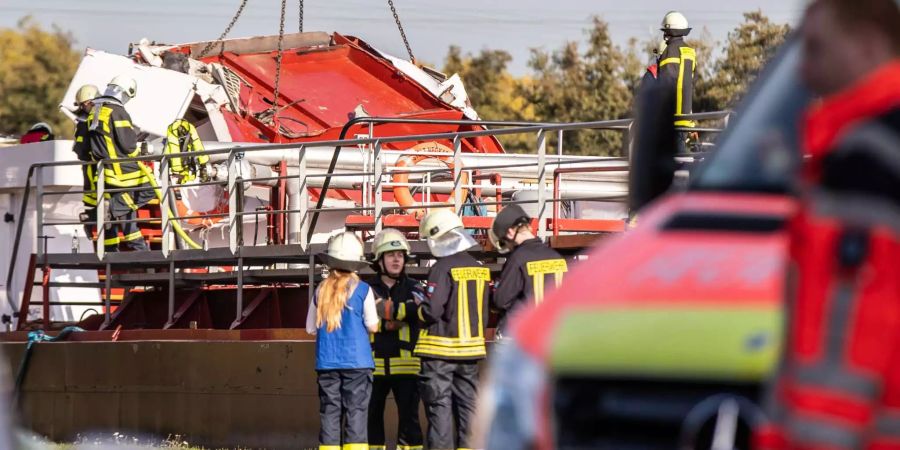 Feuerwehrleute versuchen mit der Hilfe eines Kranes, das zerstörte Steuerhaus eines Frachtschiffes anzuheben.