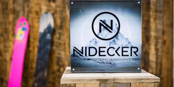 Zwei Snowboards stehen neben dem Firmenlogo der Nidecker-Gruppe. Zwei Snowboards stehen neben dem Firmenlogo der Nidecker-Gruppe.