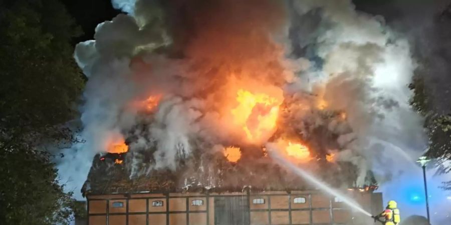 Feuerwehrleute löschen das Feuer in der mit Reet gedeckten Museumsscheune. Foto: -/TNN/dpa