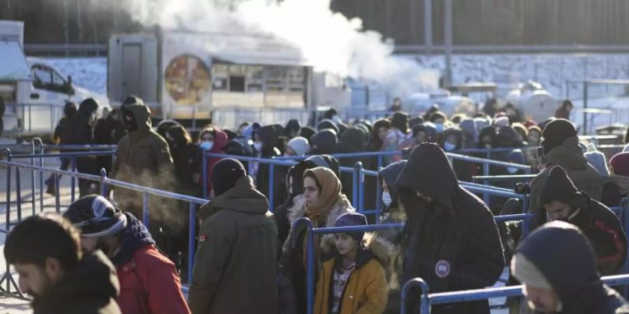 Migranten stehen in der Nähe eines Logistikzentrums an der polnisch-belarussischen Grenze an einer Essensausgabe an. Foto: Pavel Golovkin/AP/dpa