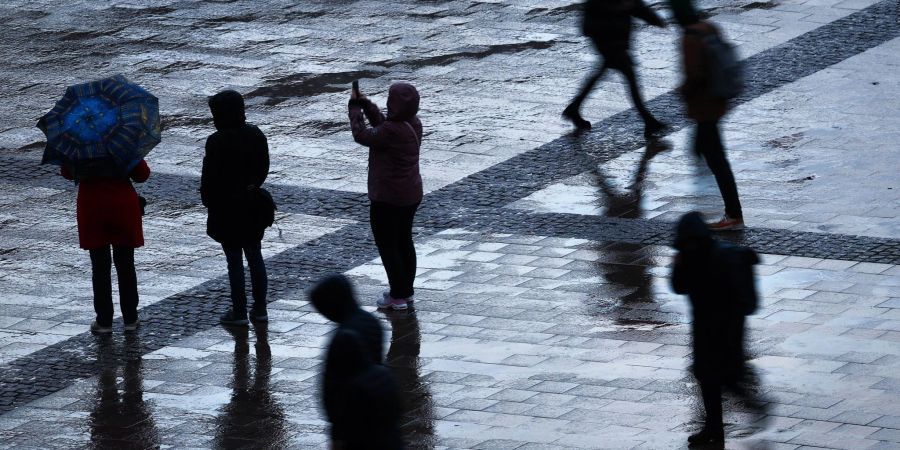 Passanten gehen bei Regen und Sturm über den Rathausplatz in der Innenstadt.