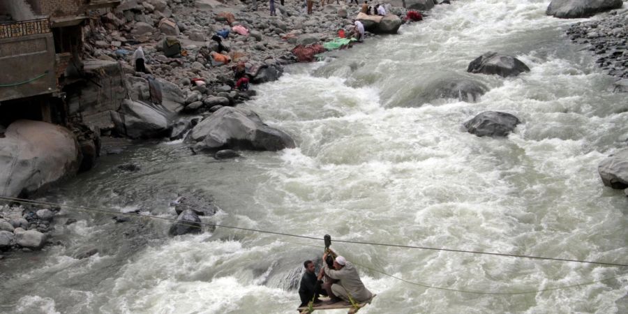 Nach schweren Überschwemmungen überqueren Menschen im pakistanischen Bahrain einen Fluss mithilfe einer Seilbahn.