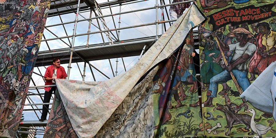 Documenta-Mitarbeiter bauen das umstrittene Grossbanner «People's Justice» des indonesischen Künstlerkollektivs Taring Padi auf dem Friedrichsplatz ab. Foto: Uwe Zucchi/dpa - ACHTUNG: Nur zur redaktionellen Verwendung im Zusammenhang mit einer Berichterstattung über die documenta 15 und nur mit vollständiger Nennung des vorstehenden Credits