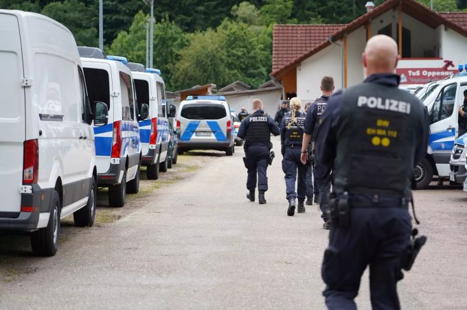 Polizisten gehen an einem Parkplatz in Oppenau an Polizeifahrzeugen vorbei. oppenau