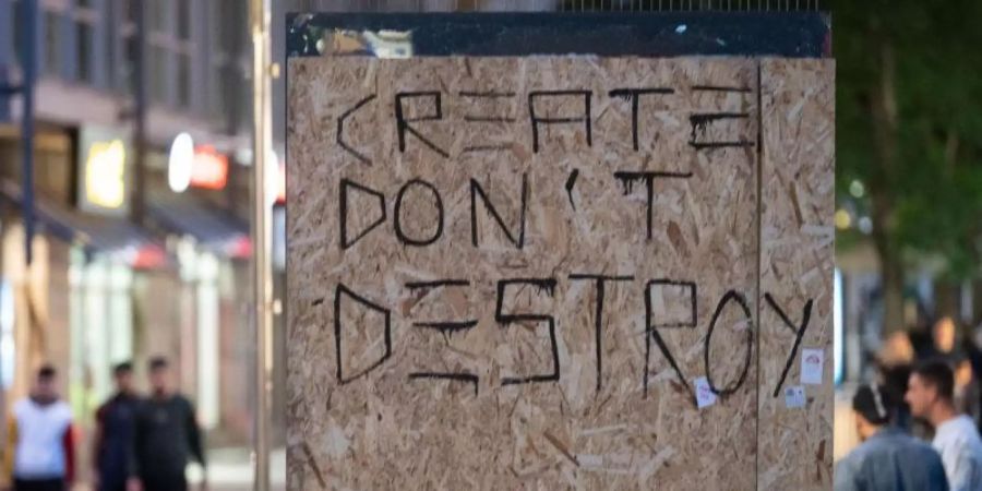 Die Worte «Create don't Destroy» (Erschaffe statt zu zerstören) stehen auf Holzplatten, mit denen in Stuttgart die beschädigte Scheibe einer Werbetafel abgedeckt worden ist. Foto: Marijan Murat/dpa