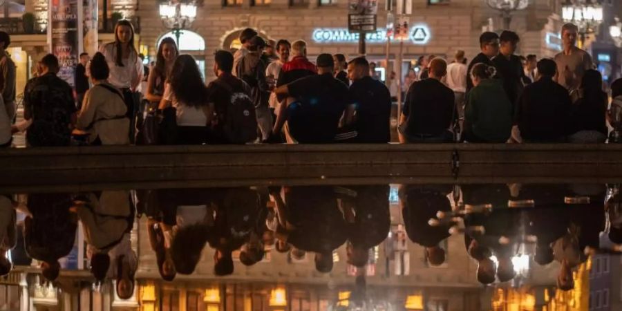 Menschen sitzen am Brunnen vor der Alten Oper in Frankfurt. Dort wurde in der Nacht nur friedlich gefeiert. Foto: Frank Rumpenhorst/dpa