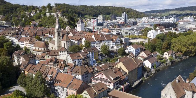 Blick auf die Badener Alt- und Neustadt mit Turm der Sebastiankapelle und des Stadtturms und der gedeckten Holzbruecke ueber der Limmat.