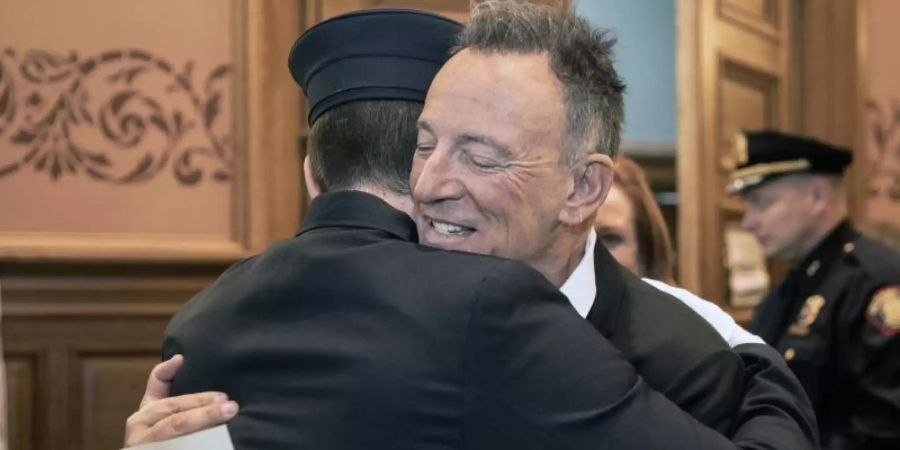 Bruce Springsteen (vorne, r), umarmt seinen Sohn Sam, nachdem dieser im Rathaus von Jersey City als Feuerwehrmann vereidigt wurde. Foto: Jennifer Brown/Jersey City Mayor's Office/AP/dpa