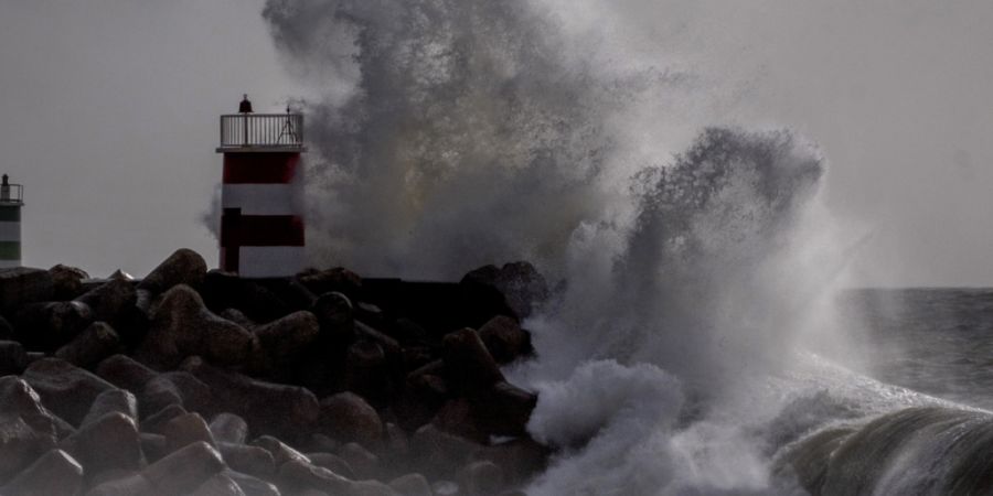 ARCHIV - Große Wellen krachen 2024 gegen einen Leuchtturm bei Nazaré an der Küste Portugals. Foto: Michael Probst/AP/dpa