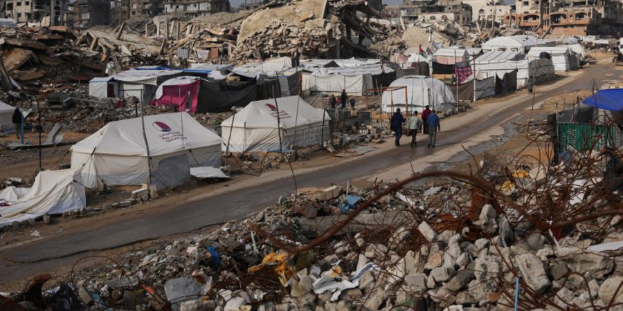 Palästinenser gehen eine Straße entlang, vorbei an einem Zeltlager, das von Gebäuden umgeben ist, die bei israelischen Luft- und Bodenoperationen im Viertel Sheikh Radwan zerstört w...