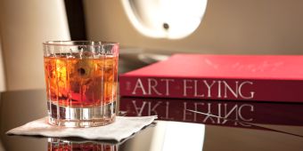 Buch The Art of Flying neben Whiskeyglas im Flugzeug.