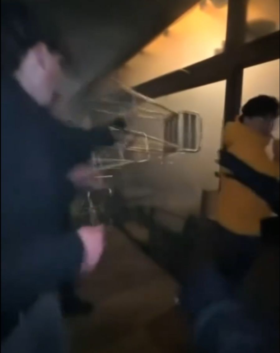 Junge Männer versuchen, mit Stühlen die Scheibe einzuschlagen.