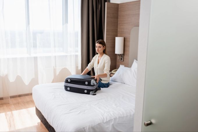 Manchmal lohnt sich ein Upgrade des Zimmers, um einen ruhigen Raum abseits des Lärms zu bekommen. Frau im Hotel mit Koffer auf dem Bett