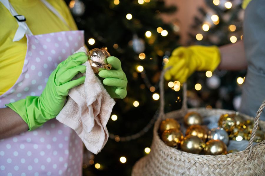 Frau reinig Weihnachtsbaumschmuck mit Tuch und Handschuhen