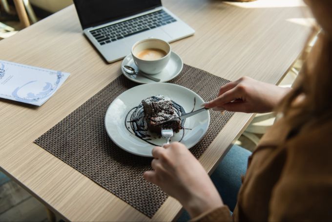 Der gelegentliche Schokokuchen macht nicht dick, Süssigkeiten in Übermassen schon. Frau isst Schokoladenkuchen am Computer.