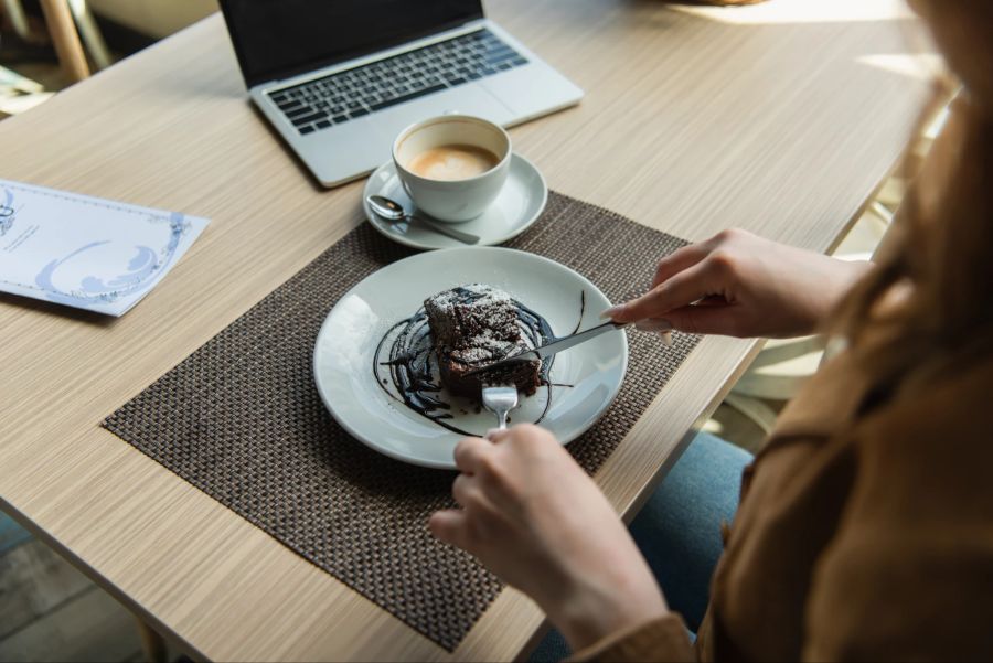 Frau isst Schokoladenkuchen am Computer.