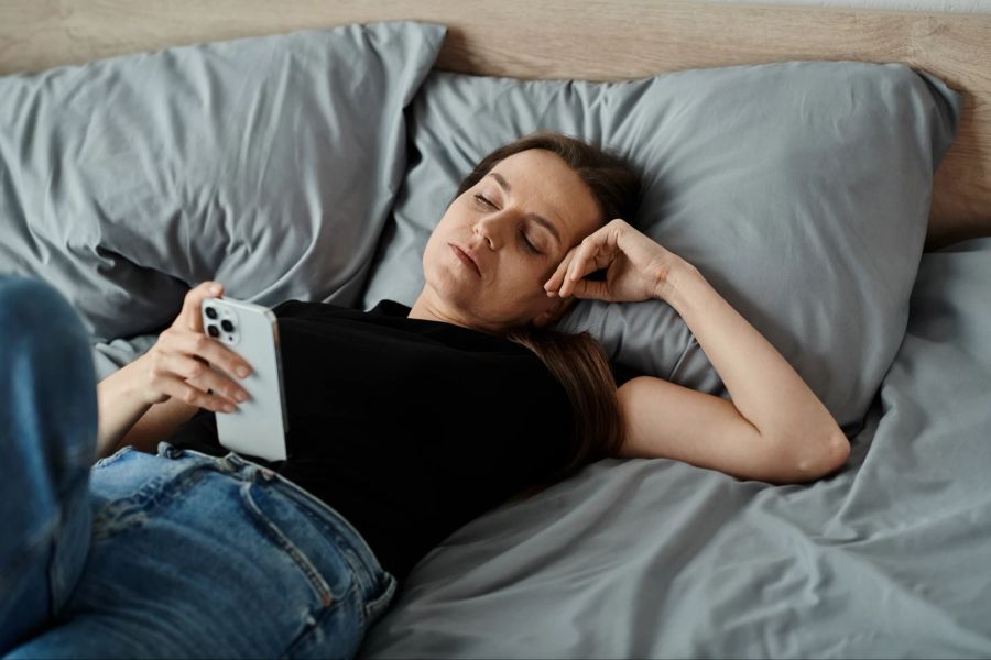 Müde Frau mit Smartphone liegt im Bett