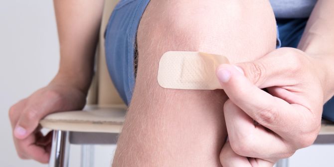 Eine Person zieht Pflaster vom Knie ab
