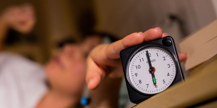 Eine Frau schaltet vom Bett aus einen auf sechs Uhr gestellten Wecker aus.