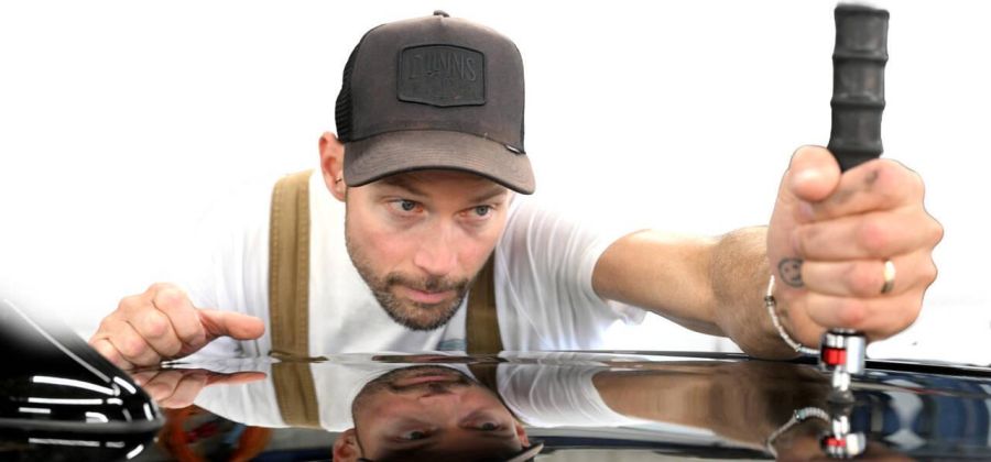 Marc Rösch zieht eine Hagelbeule aus einem Dachblech. Einige der Autos, die er aktuell repariert, hatte er bereits nach dem Hagel im Frühling bearbeitet.
