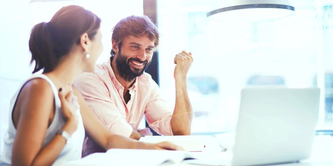 mann und frau, lachend an tisch, schauen auf laptop