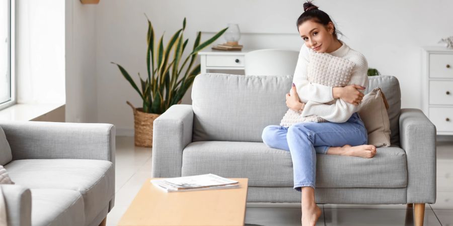 Junge Frau sitzt mit Kissen auf kleiner Couch