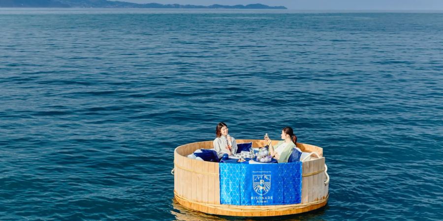 Schwimmendes Holzfloss im Meer mit zwei Japanerinnen mit Mikrofon.