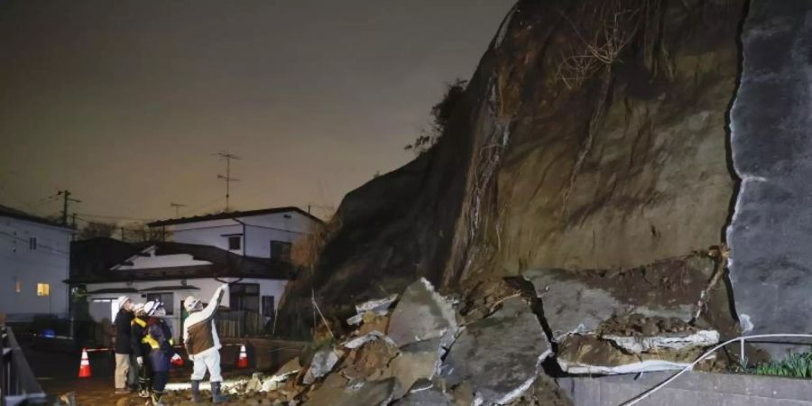 Menschen stehen vor eingestürzten Teilen einer Klippe. Eine Tsunami-Warnung in Folge eines starken Erdbebens im Nordosten Japans ist wieder aufgehoben worden. Foto: ---/Kyodo/dpa