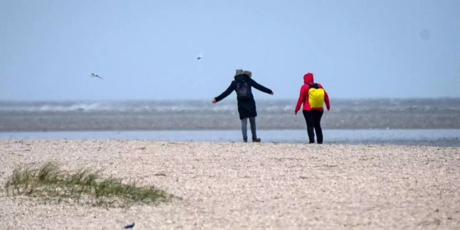 Spaziergänger laufen bei windigen Wetter über einen Strand in Niedersachsen. Foto: Sina Schuldt/dpa