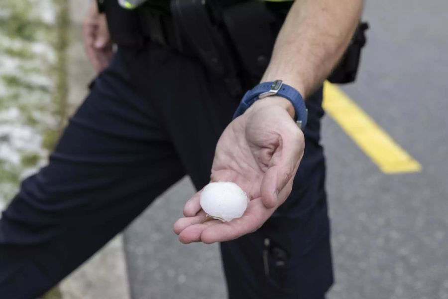 Ein Polizist hält ein Hagelkorn in Bulle FR. Diese Woche ist es vermehrt zu Regen und Hagel gekommen.