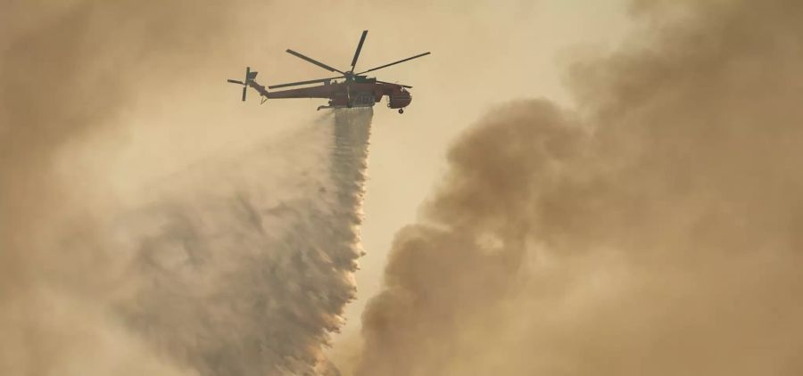 Ein Hubschrauber wirft Wasser über einem Waldbrand im Gebiet Varibobi im Norden Athens ab.