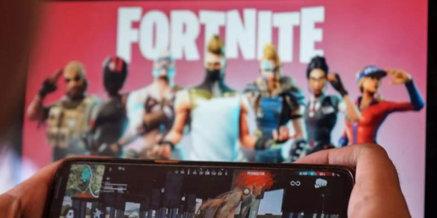 Ein Kind spielt ein Spiel auf einem Mobiltelefon mit einem Bild des Fortnite-Spiels auf dem Computerbildschirm im Hintergrund. (Archivbild). Foto: Herwin Bahar/ZUMA Wire/dpa