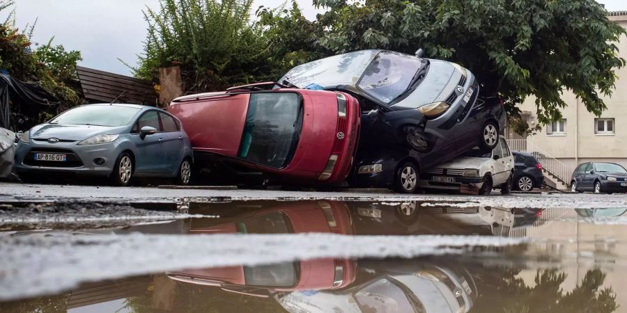 Beschädigte Autos, die teilweise übereinander liegen,  spiegeln sich am Tag nach dem Hochwasser in Trebes (F) im Wasser.