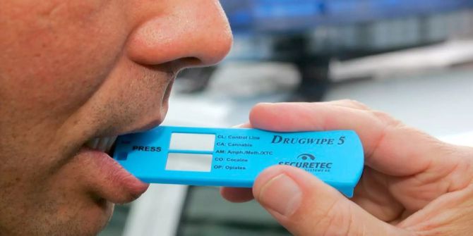 An einem Polizeimitarbeiter wird die Anwendung des Drogenschnelltest-Gerätes demonstriert.