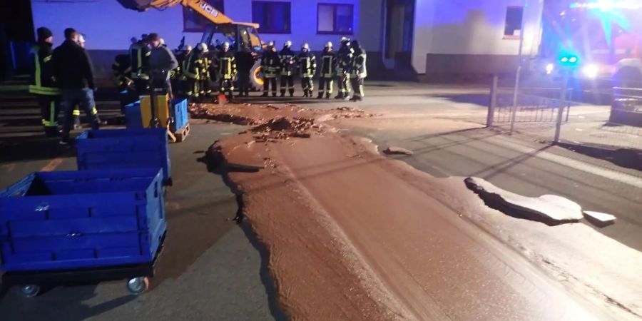 Einsatzkräfte der Feuerwehr stehen neben auf der Strasse ausgelaufener Schokolade.