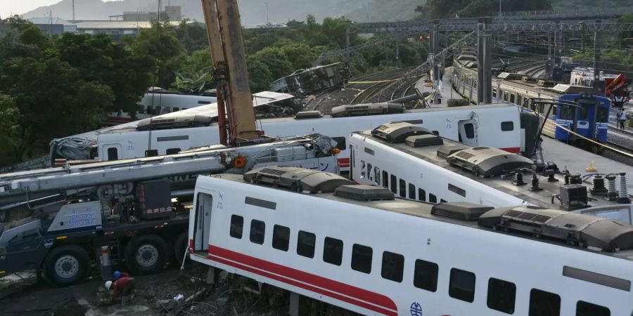 Ein Zug (rechts) passiert entgleiste Zugwaggons, die neben den Gleisen stehen und liegen.