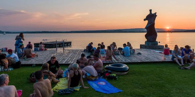 Badende beim Holzrost des Seebads Seeliken Menschen geniessen den Sonnenuntergang am Seebad Seeliken