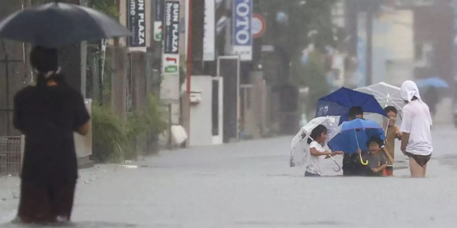 Menschen waten durch eine überflutete Strasse in Kurume, Westjapan. Sintflutartige Regenfälle suchten den Südwesten Japans seit Freitag heim und forderten mindestens sechs Todesopfer. Nach einer Unterbrechung regnete es am Montagmorgen (Ortszeit) auf der südwestlichen Hauptinsel Kyushu erneut stark. Foto: Kyodo News/via AP/dpa - ACHTUNG: Nur zur redaktionellen Verwendung und nur mit vollständiger Nennung des vorstehenden Credits