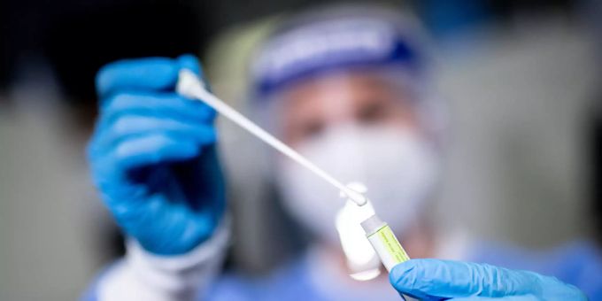 Eine Frau hält die Probe von einem Rachenabstrich in den Händen. coronavirus