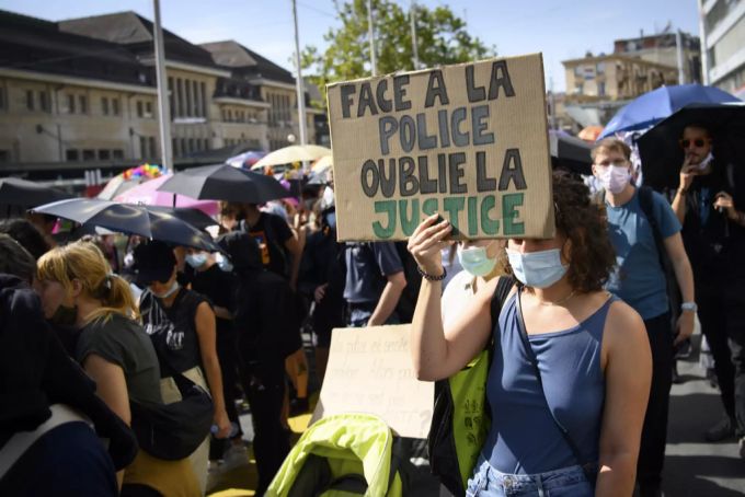 Eine Demonstrantin hält ein Schild mit der Aufschrift «Vor der Polizei vergiss die Gerechtigkeit» auf. Demo Lausanne