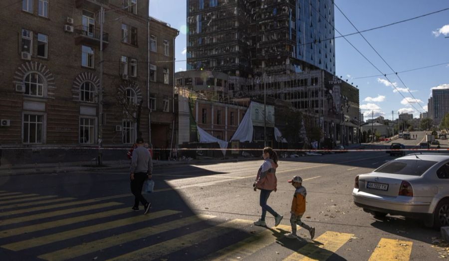 Menschen gehen an von russischen Raketen zerstörten Gebäuden in der ukrainischen Hauptstadt Kiew vorbei.