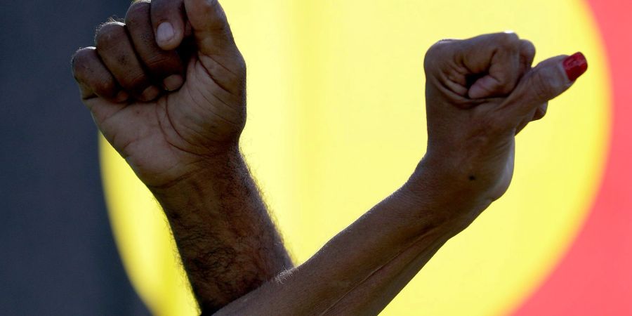 Während einer Kundgebung in Sydney verschränken  zwei Demonstranten vor einer Aborigine-Flagge ihre Arme.