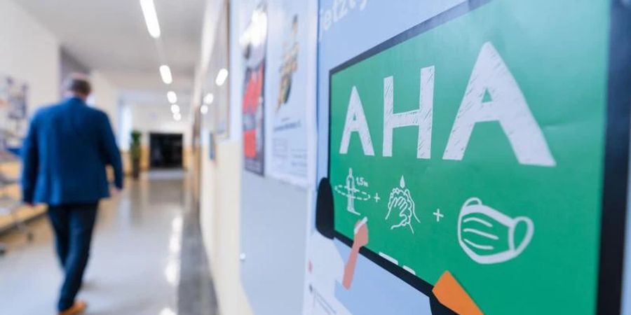 An der Wand eines Flurs in einem Gymnasium ist ein Hinweis auf die AHA-Regeln angebracht. Das Infektionsrisiko ist durch Omikron gerade extrem hoch. Foto: Nicolas Armer/dpa