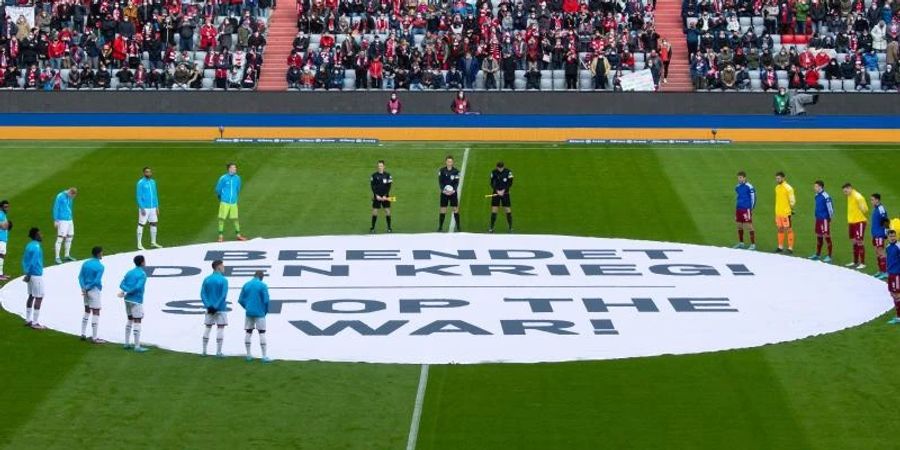 Die Spieler von München und von Leverkusen stehen um ein Banner mit «Beendet den Krieg! - Stop the War!». Foto: Sven Hoppe/dpa