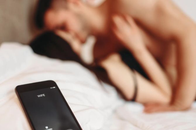 Mann und Frau intim im Bett, Smartphone im Vordergrund