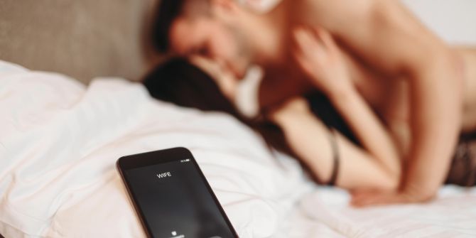 Mann und Frau intim im Bett, Smartphone im Vordergrund
